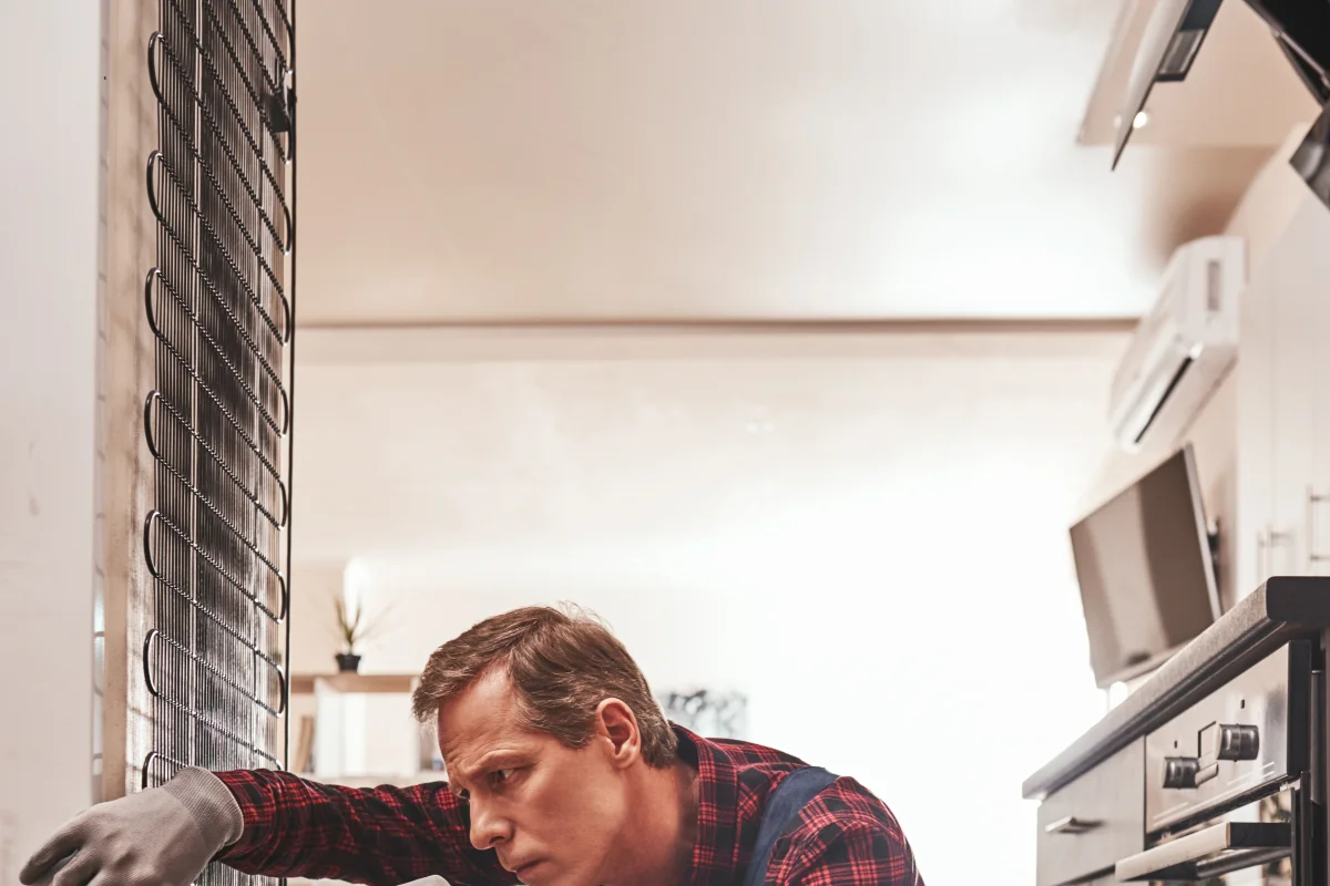 appliance-repair-north-phoenix-refrigerator-technician Appliance repair in North Phoenix, Arizona — a technician in a plaid work shirt and gloves inspecting the coils of an open refrigerator.