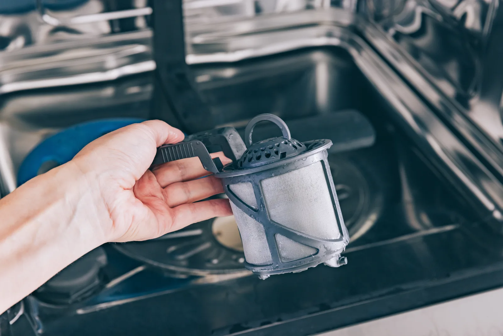 asko-dishwasher-repair-phoenix-mineral-scale-filter-cleaning A hand removing an Asko dishwasher's sump filter to clear mineral scale buildup caused by Phoenix's hard water.