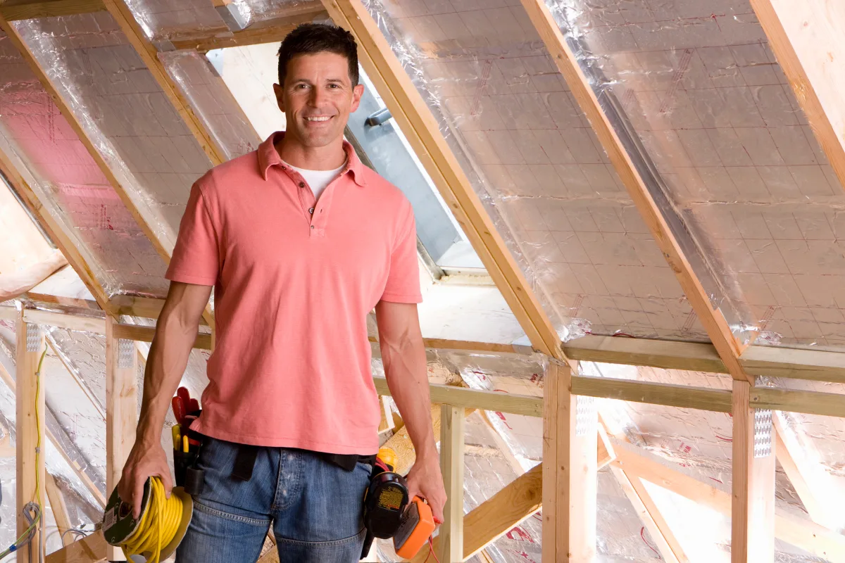 attic-insulation-phoenix-attic-install Attic insulation in Phoenix, Arizona — a contractor in a collared work shirt standing in an attic with radiant barrier insulation installed along the rafters.