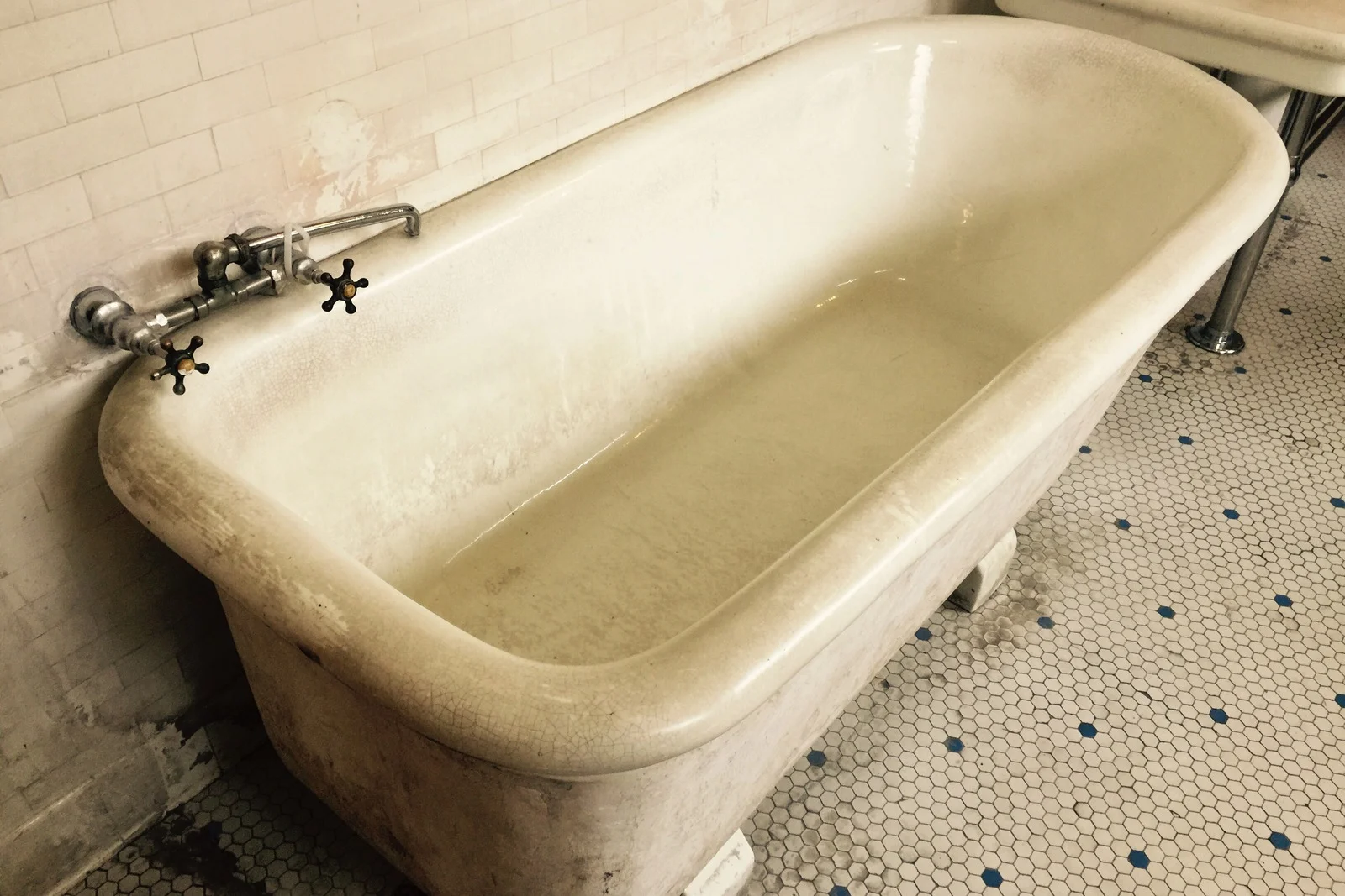 bathtub-refinishing-phoenix-worn-tub-before A worn, stained cast-iron bathtub in an older Phoenix home before refinishing, showing the kind of hard-water etching and age that refinishing corrects.