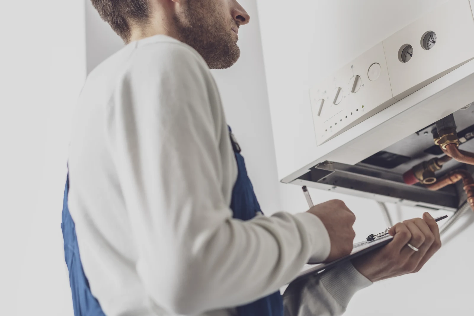 A boiler repair technician reviewing an inspection checklist on a clipboard in front of an open wall-mounted boiler in a Phoenix home.