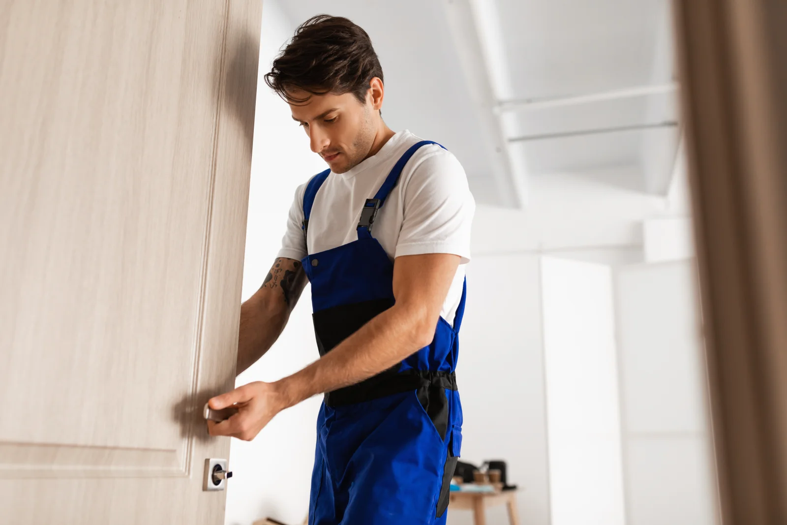 Broken key extraction in Phoenix, Arizona — a locksmith in blue work overalls examining a residential door lock and handle.