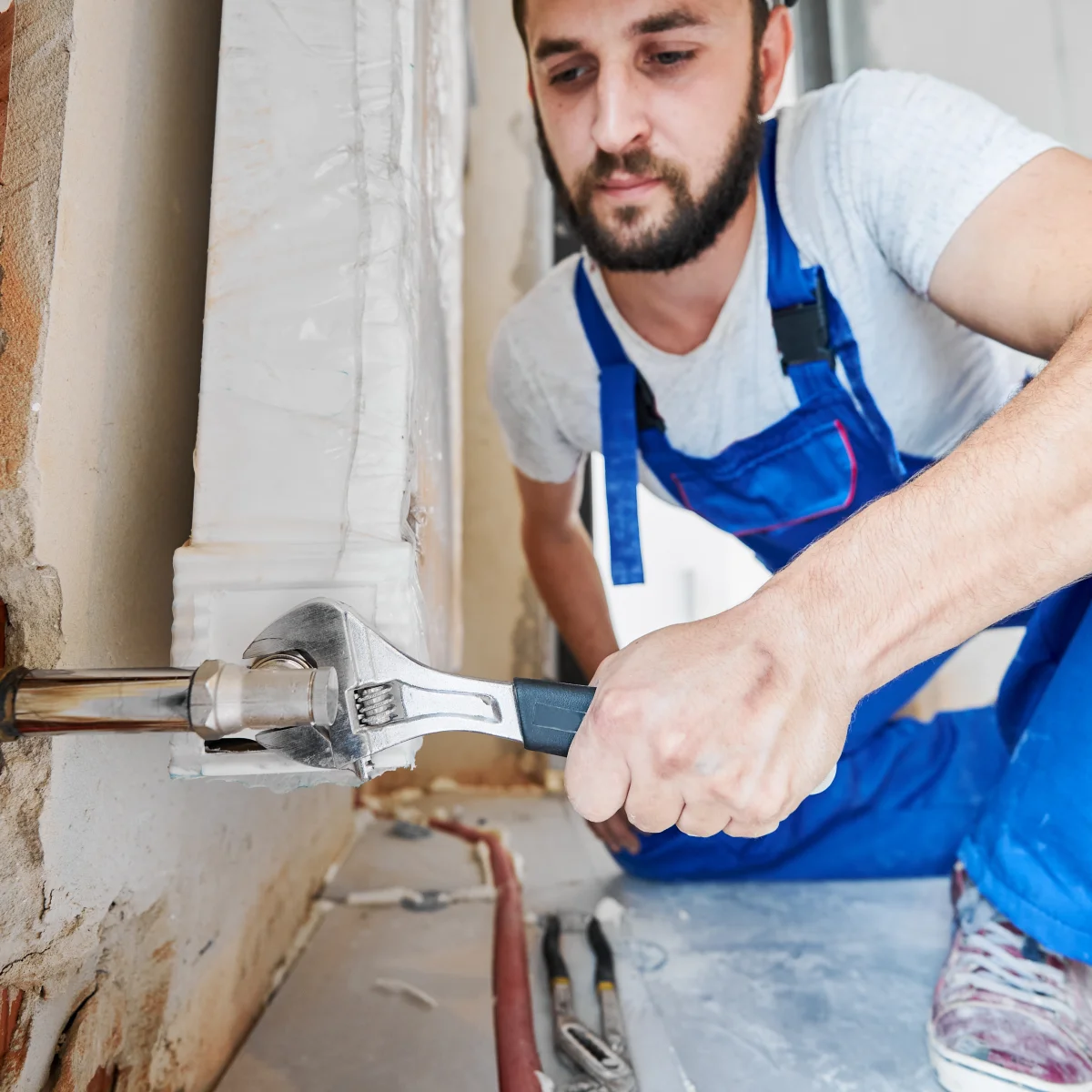 burst-pipe-repair-phoenix-emergency-plumber Burst pipe repair in Phoenix, Arizona — a plumber using a wrench to repair a broken water pipe exposed in a home wall.