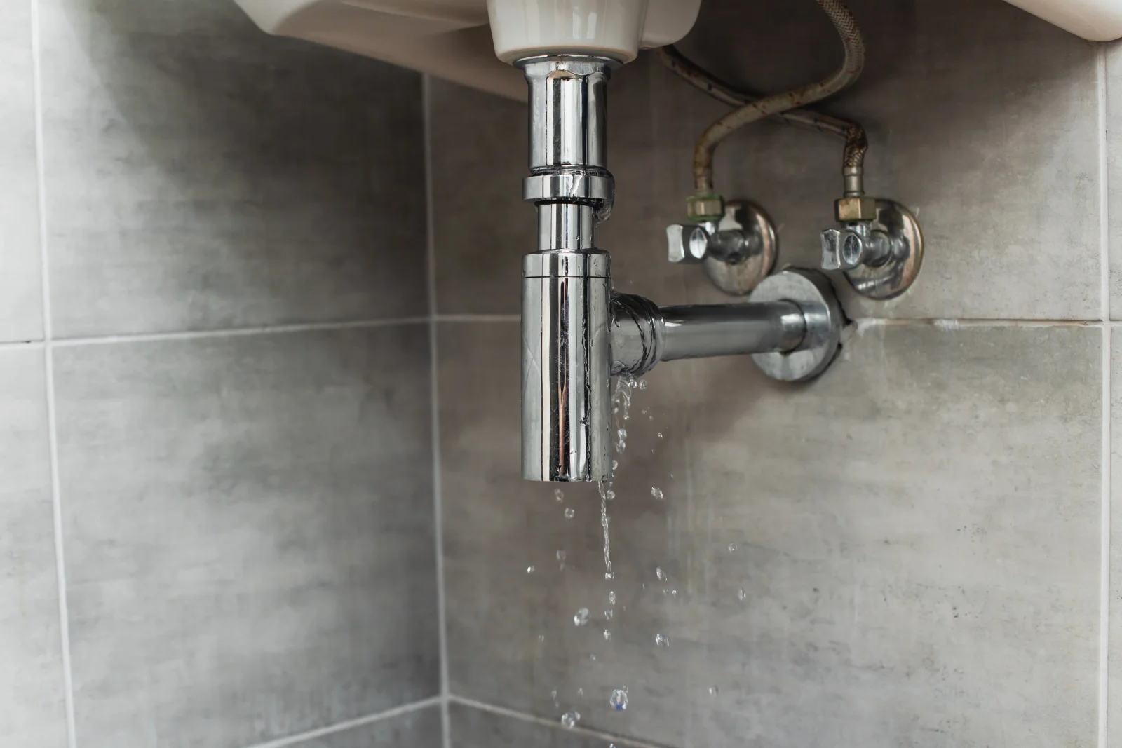 burst-pipe-repair-phoenix-leaking-pipe-fitting A corroded water pipe fitting leaking and dripping under a sink in a Phoenix home, the kind of aging, corroded connection that can fail and burst without warning if left unrepaired.