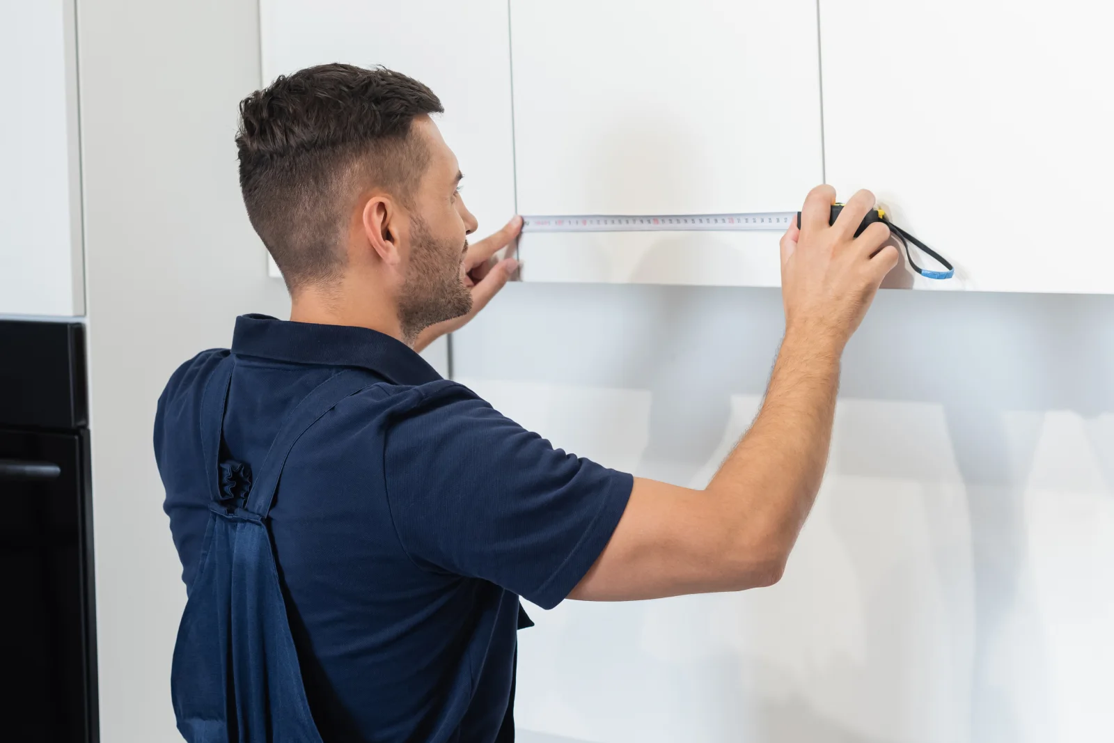 cabinet-painting-phoenix-prep-precision A professional in a navy work uniform precisely measuring kitchen cabinet doors before painting, the kind of prep work that keeps a Phoenix cabinet paint job from failing early.