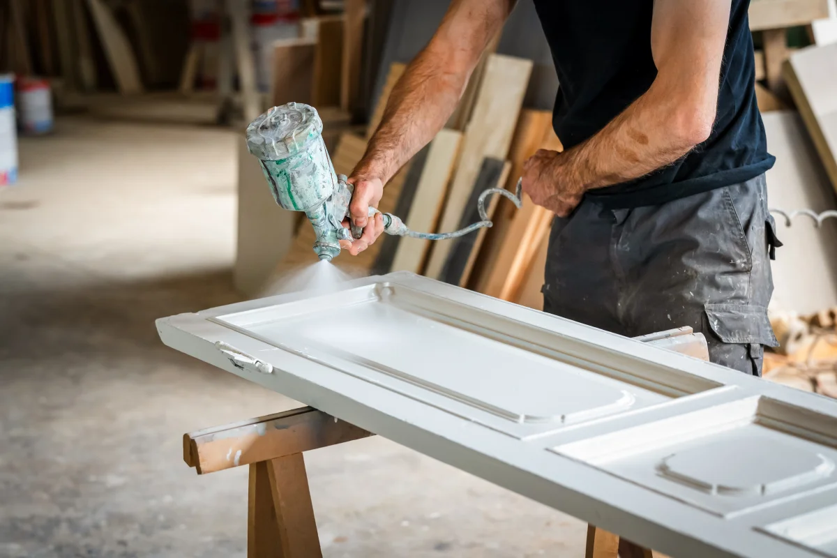 cabinet-refinishing-phoenix-az-spray-finish Cabinet refinishing in Phoenix, AZ — a professional carpenter using a spray gun to apply finish to a cabinet door in a workshop.
