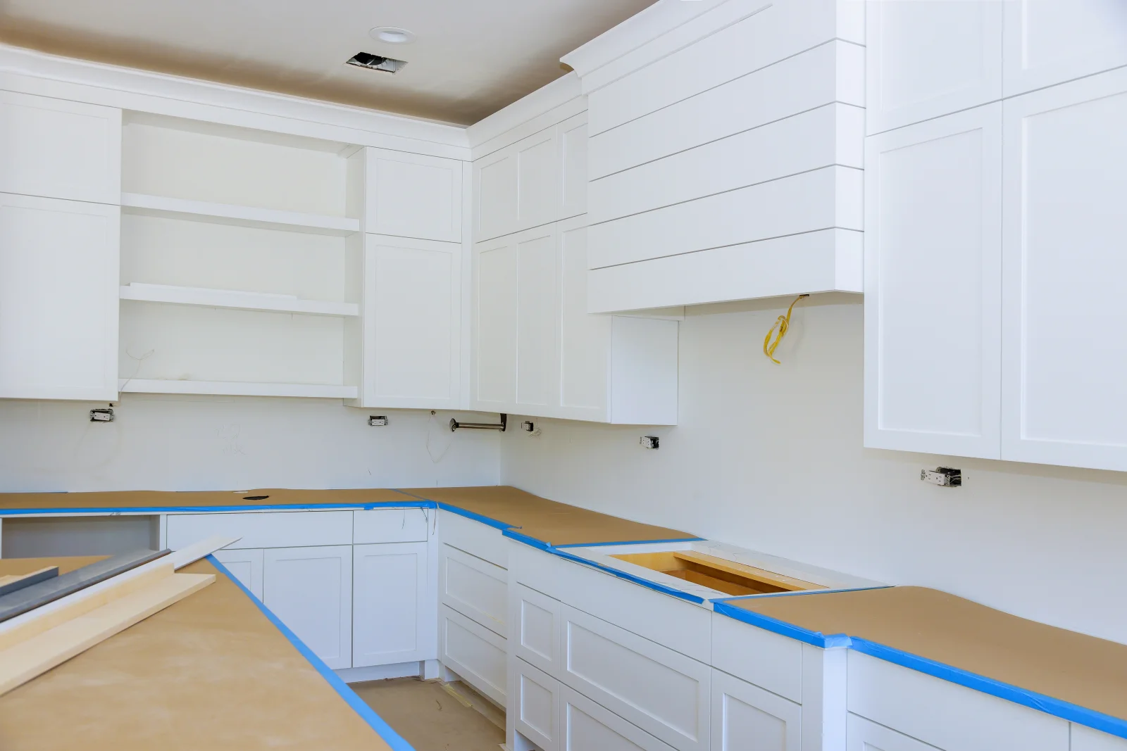cabinet-refinishing-phoenix-az-kitchen-prep Cabinet refinishing in Phoenix, AZ — new and refinished kitchen cabinets mid-installation with blue painter's tape and protective paper on the counters.