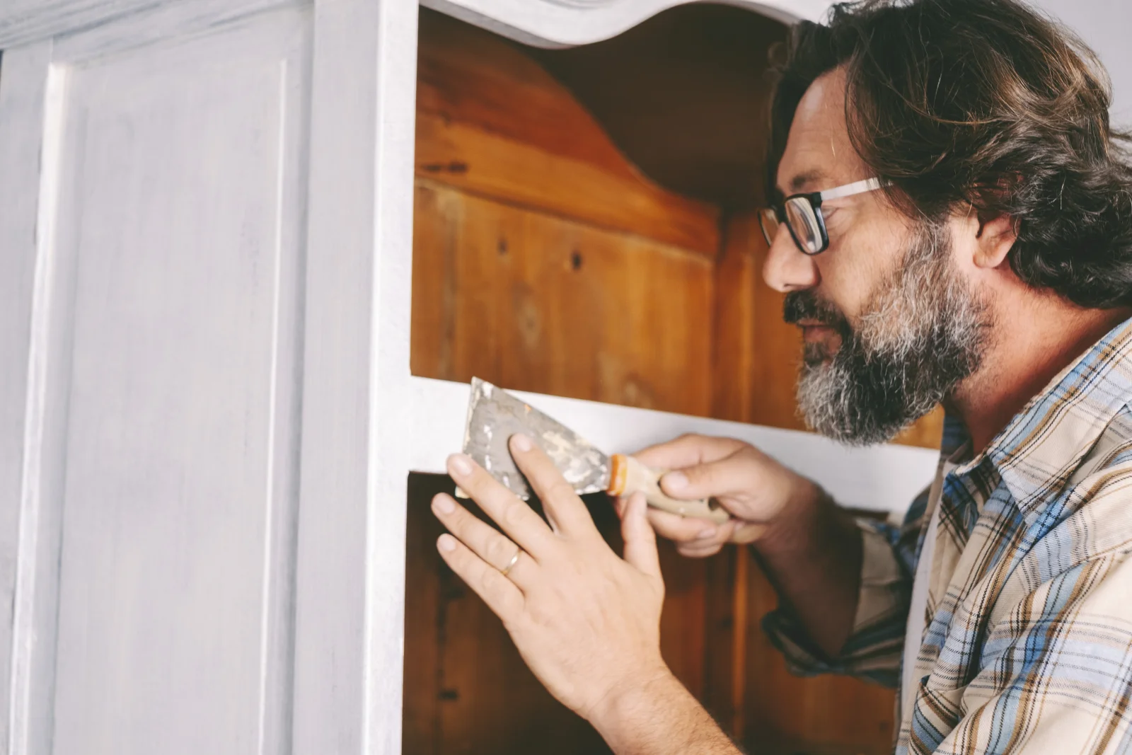 cabinet-refinishing-phoenix-az-wood-filler-repair Cabinet refinishing in Phoenix, AZ — a close-up of a craftsman applying wood filler to a cabinet surface with a putty knife before refinishing.