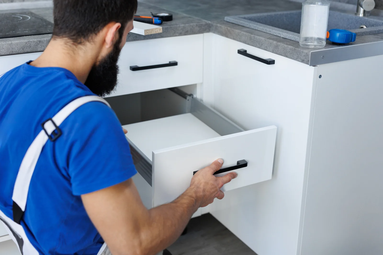 cabinet-repair-phoenix-drawer-repair A cabinet repair technician in a work uniform checking a kitchen drawer glide in a Phoenix home.