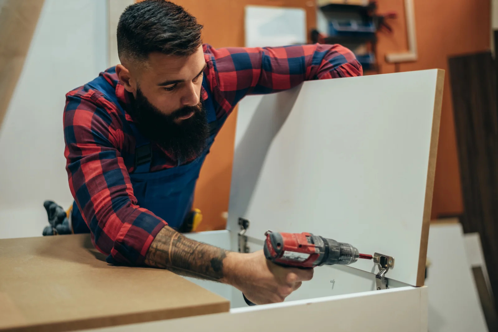 cabinet-repair-phoenix-hinge-repair A cabinet repair technician using a drill to adjust a hinge on a white kitchen cabinet door in Phoenix.