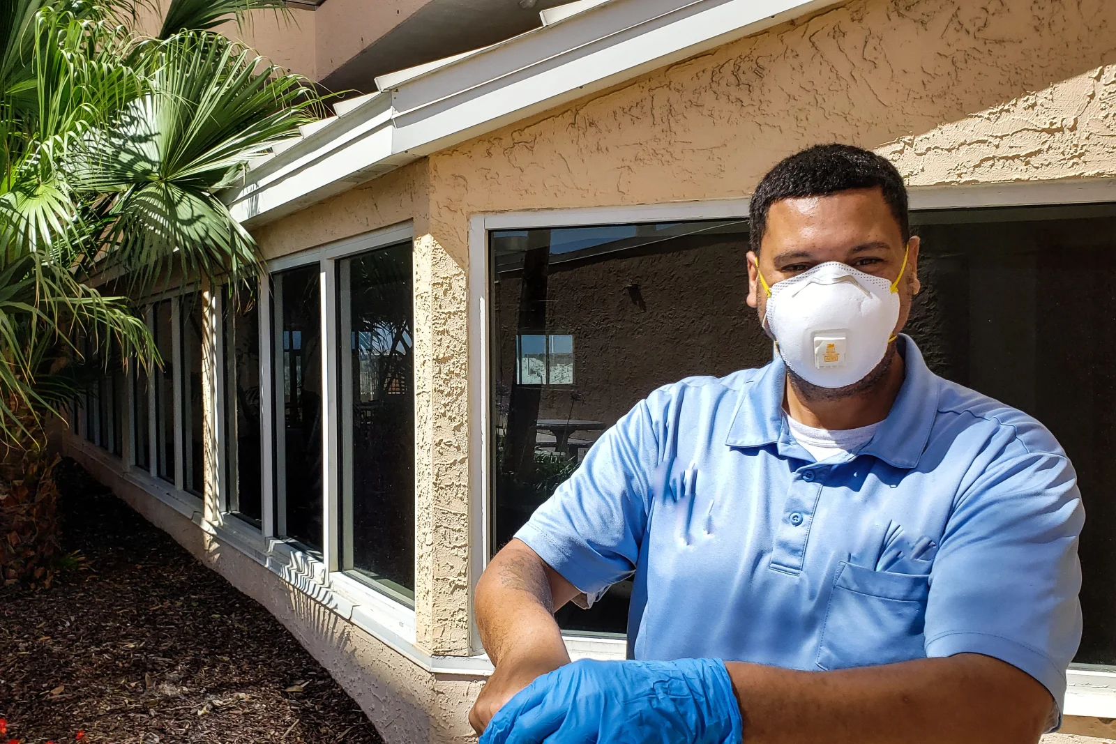 Carpenter ant control in Phoenix, Arizona — a pest control technician in a mask and gloves inspecting the exterior of a stucco home.