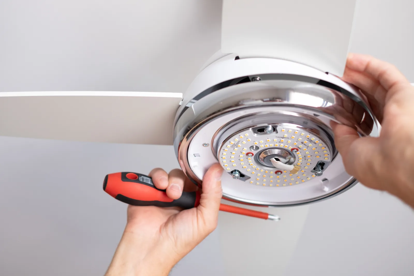 Ceiling fan repair in Phoenix, Arizona — a technician's hands wiring the light kit assembly onto a ceiling fan during a repair.