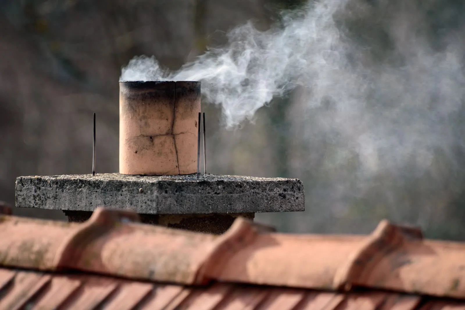 chimney-cleaning-phoenix-az-creosote-smoke Smoke rising from a chimney cap on a tile roof, showing the creosote and soot buildup that Phoenix chimney cleaning removes.