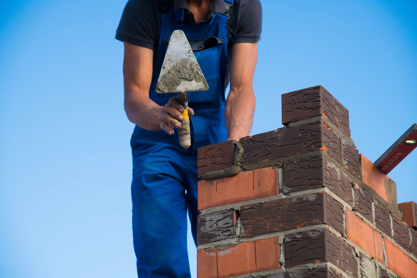 Chimney repair in Phoenix, Arizona — a mason repointing mortar joints on a brick chimney with a trowel.