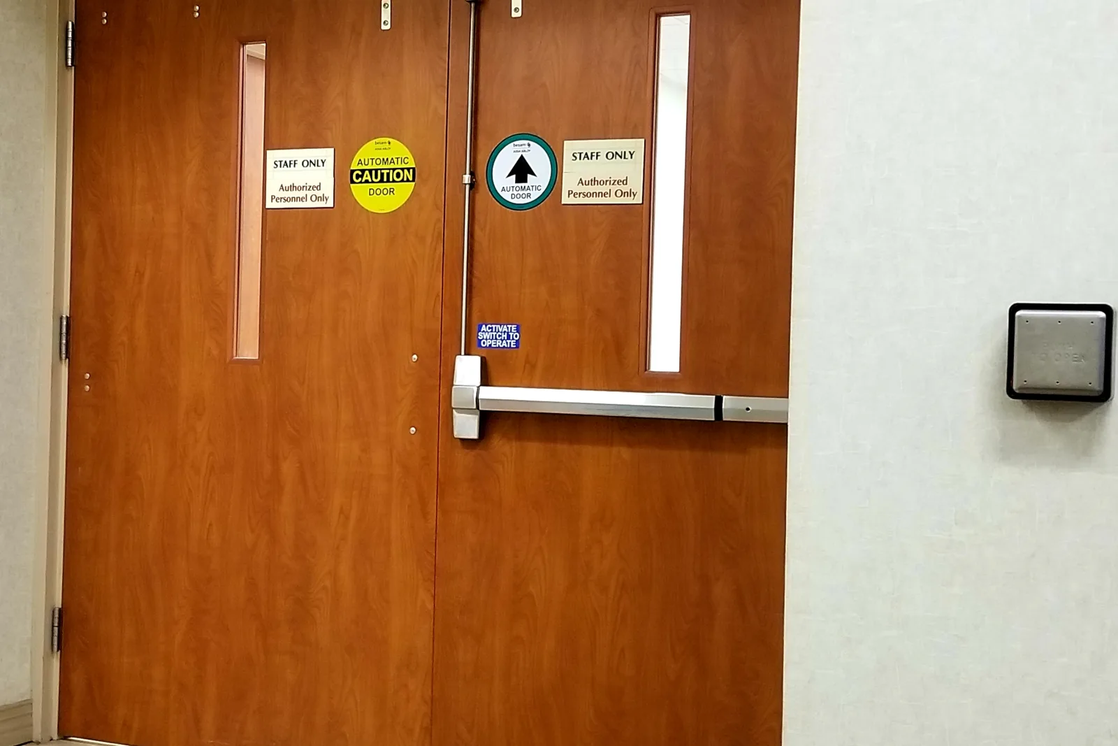 A panic bar exit device installed on a pair of commercial fire-rated doors in a Phoenix office hallway, with an access-control reader mounted on the adjacent wall.