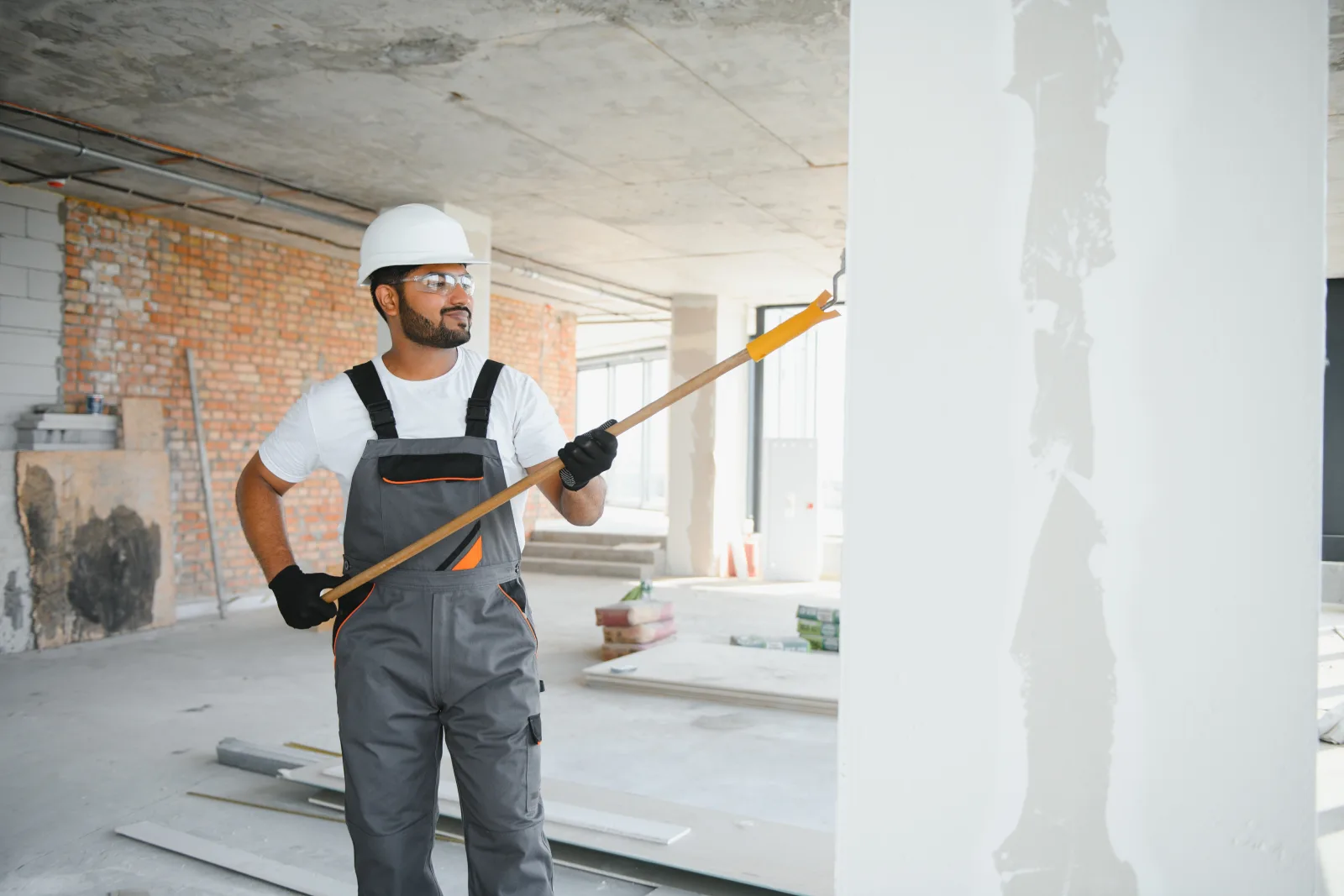 A commercial painter in a hard hat and coveralls priming an interior column before painting a Phoenix office build-out.