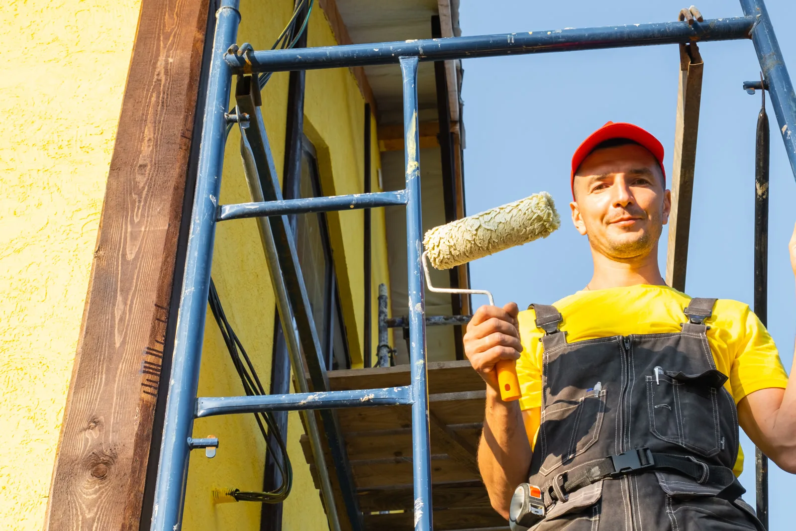 commercial-painting-companies-phoenix-safety-prep A painting contractor on scaffolding applying exterior paint with a roller to a Phoenix commercial building.