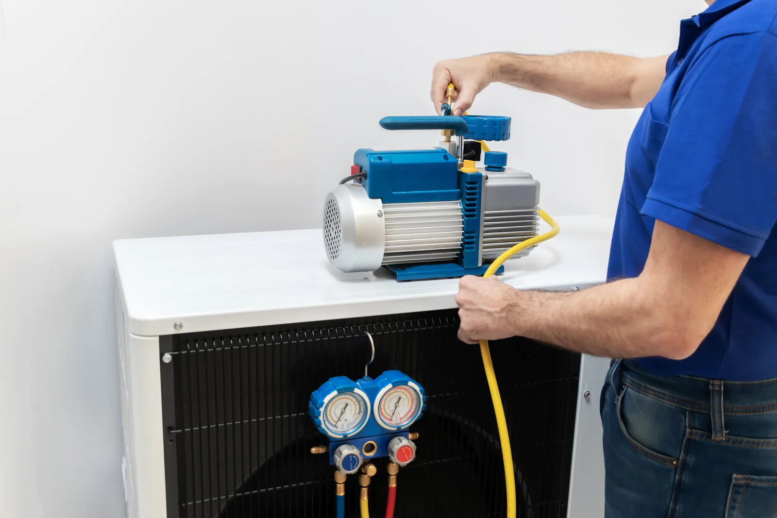 commercial-refrigeration-repair-phoenix-refrigerant-check A commercial refrigeration technician in a branded uniform using a manifold gauge set and vacuum pump to check refrigerant charge on a Phoenix business's refrigeration unit.