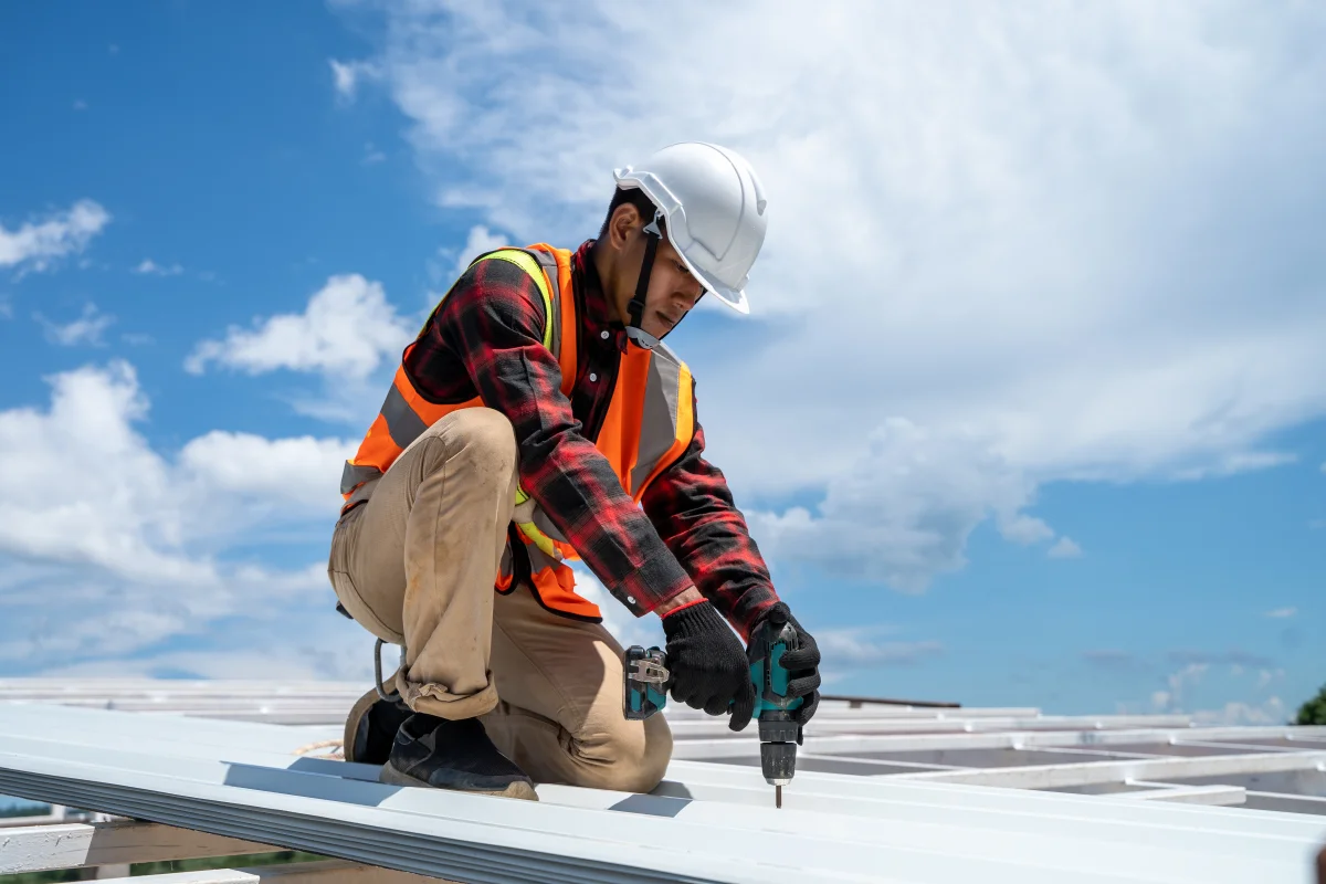 commercial-roof-replacement-phoenix-contractor Commercial roof replacement in Phoenix, Arizona — a roofing contractor in a hard hat and safety vest fastening a new commercial roof deck.