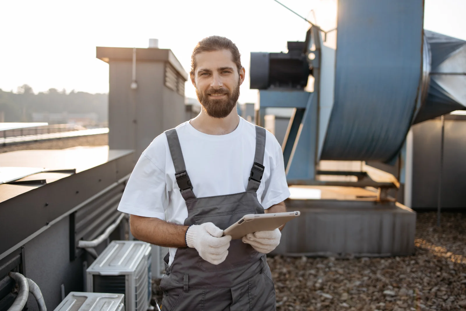 commercial-roof-replacement-phoenix-inspection A roofing technician reviewing an inspection checklist on a tablet next to rooftop HVAC equipment during a commercial roof replacement assessment in Phoenix.