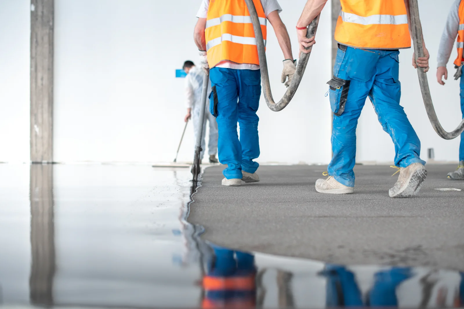 concrete-coating-phoenix-crew-prepping-self-leveling-floor A crew in safety vests carrying hoses across a freshly poured self-leveling concrete floor in Phoenix.