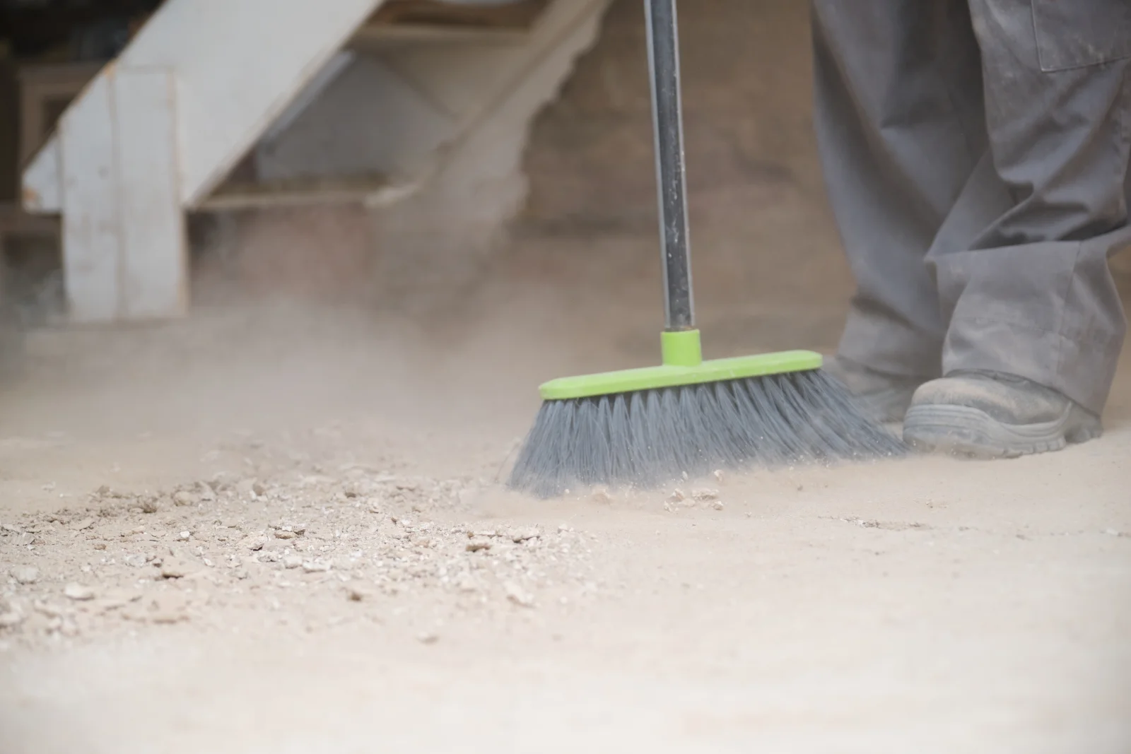 A worker sweeping fine construction dust off a concrete floor during a final cleanup pass on a Phoenix jobsite.
