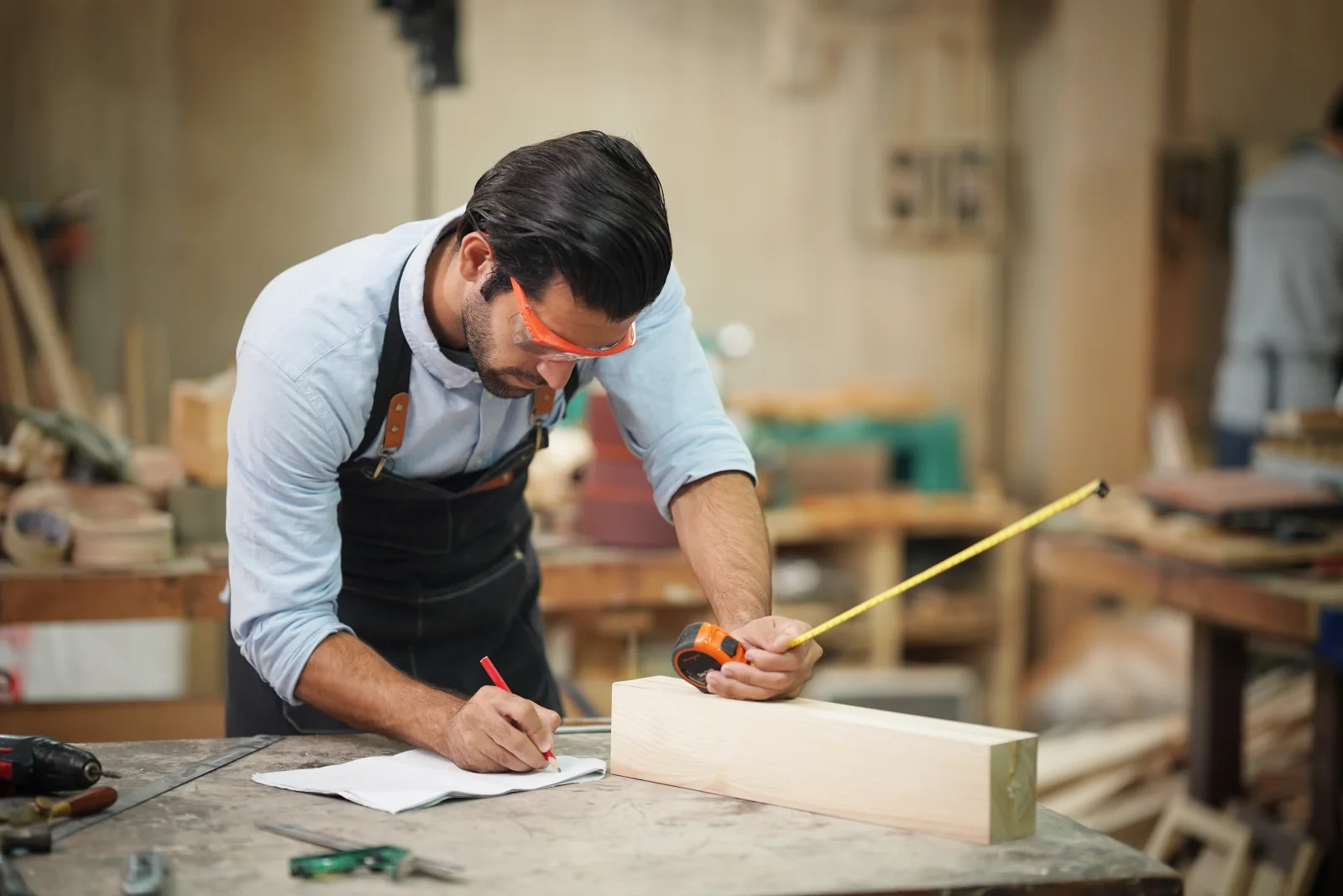 custom-furniture-phoenix-measuring-design A carpenter measuring and marking wood in a Phoenix, Arizona workshop during the design and measuring phase of a custom furniture build.