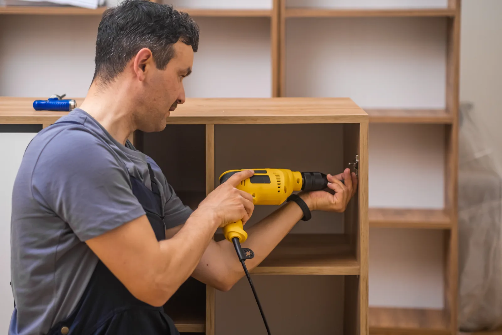 A carpenter in a Phoenix, Arizona home drilling and installing custom wood shelving into a built-in unit.