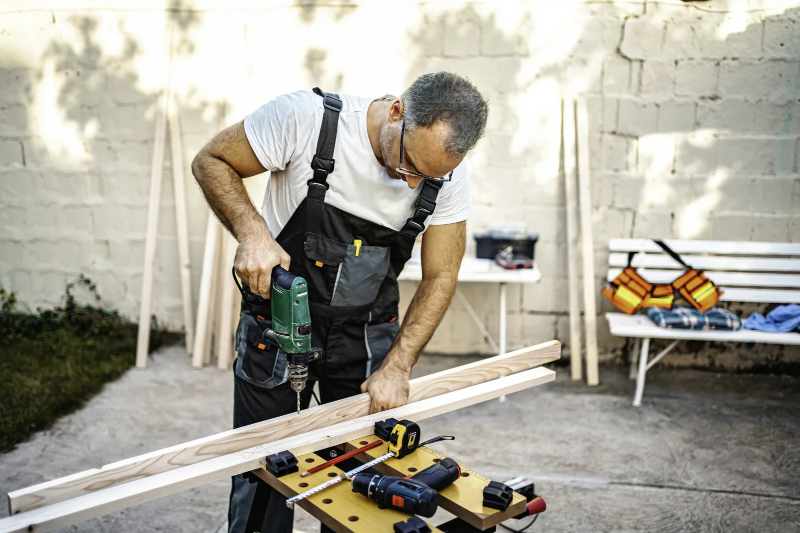 A carpenter measuring and preparing decking lumber on a workbench in a Phoenix backyard.