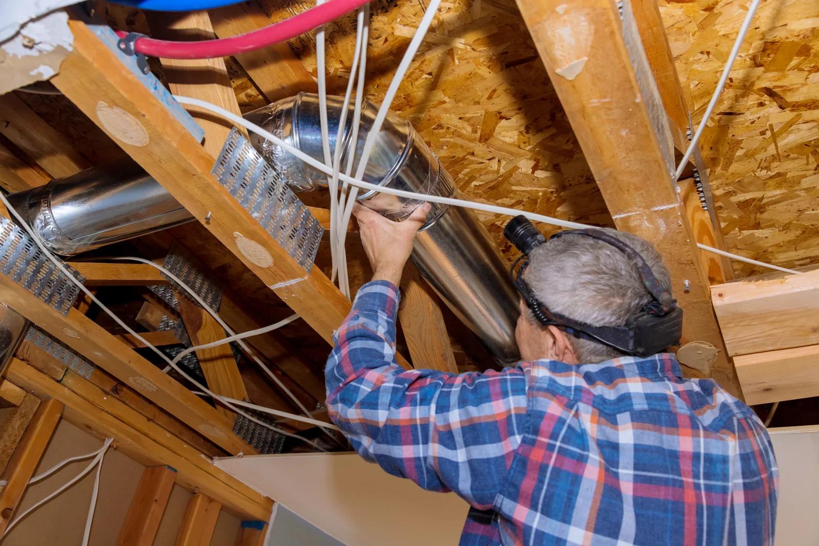 Dehumidifier installation in Phoenix, Arizona — a technician connecting a whole-home dehumidifier into insulated ductwork in an unfinished attic space.