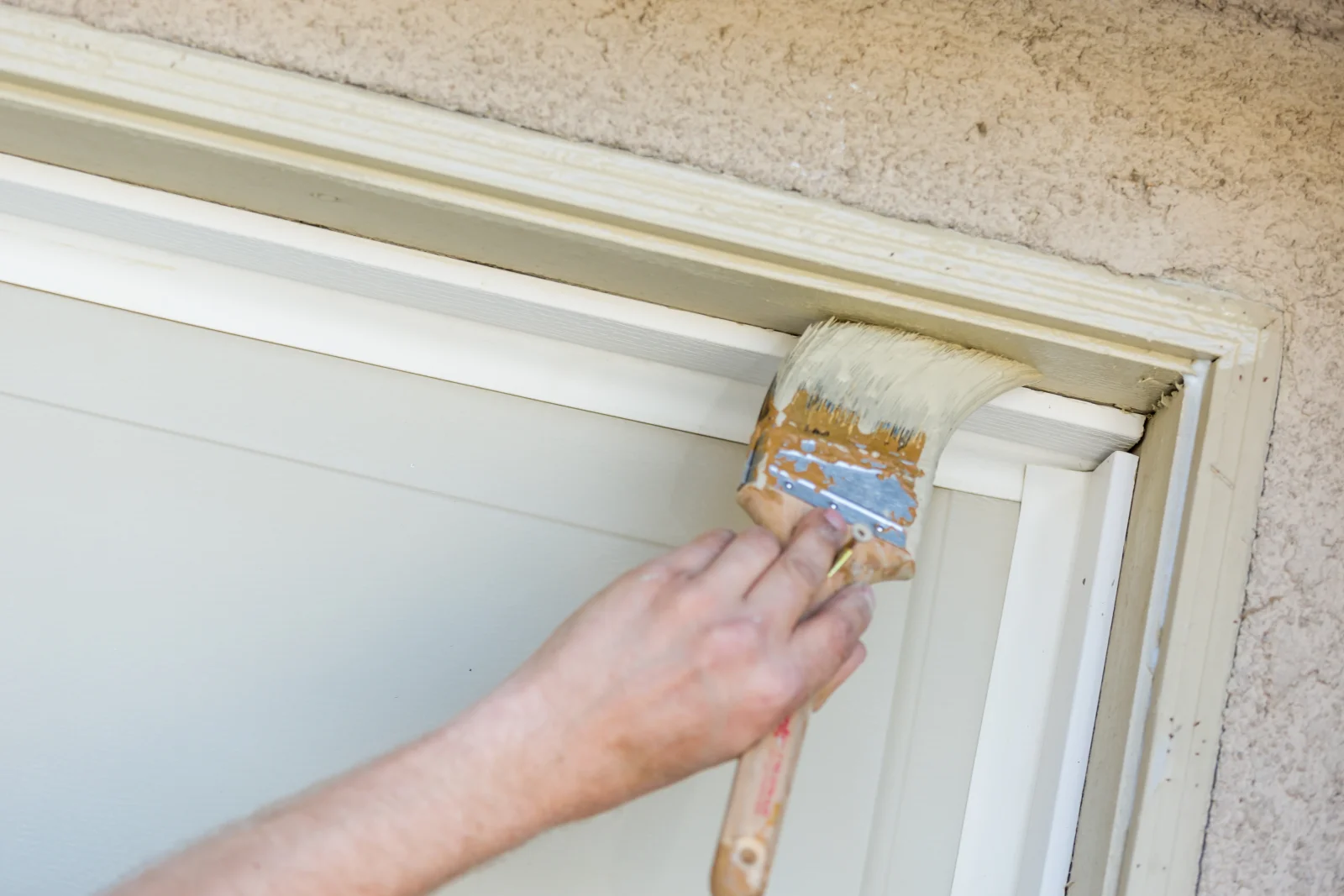 A close-up of a paintbrush applying fresh paint to a stucco-framed door trim on a Phoenix home.