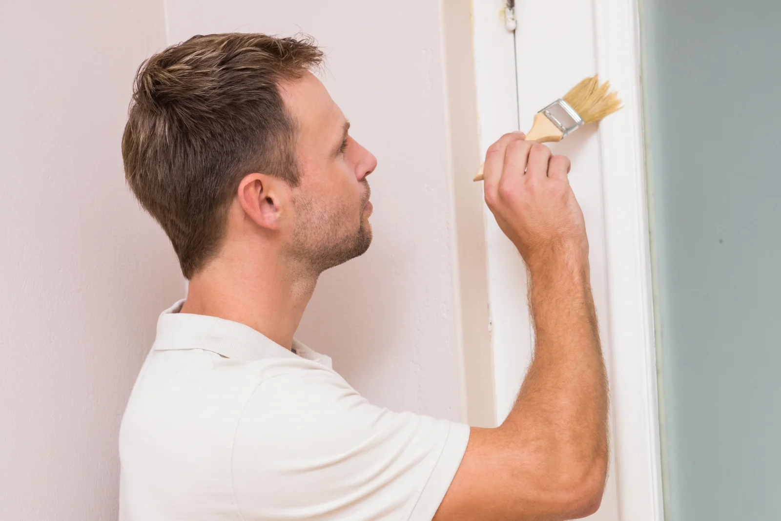 A professional brushing white paint onto a door frame trim inside a Phoenix home.