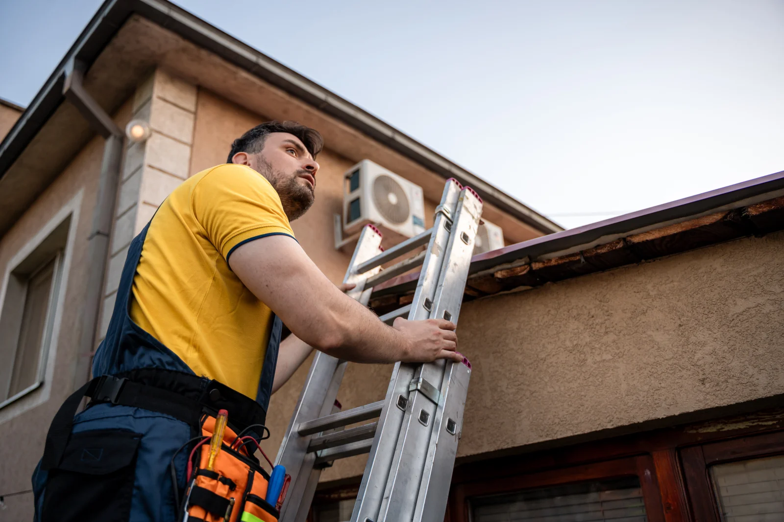 A pro on a ladder inspecting a weathered wood roofline and eave for dry rot on a Phoenix stucco home.