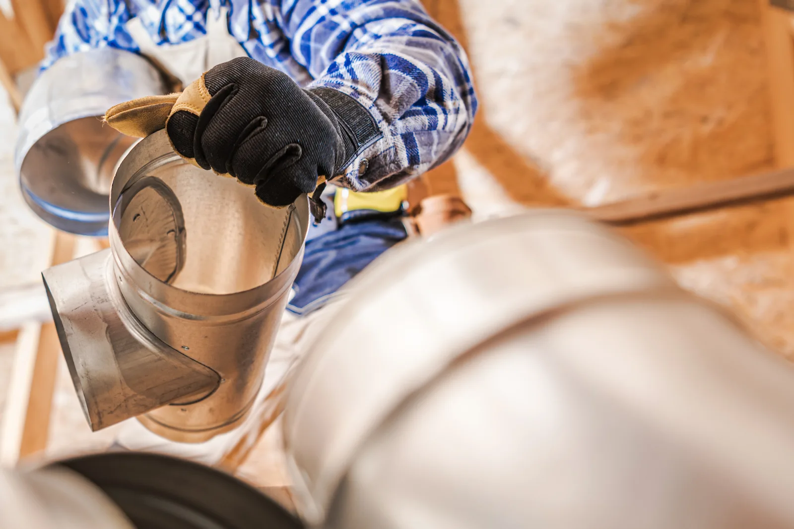 A technician fitting a rigid metal duct elbow during dryer vent installation in a Phoenix attic space.