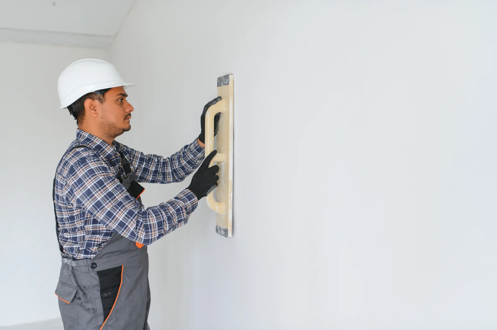 drywall-repair-phoenix-wall-patch Drywall repair in Phoenix, Arizona — a contractor in a work uniform smoothing joint compound over a patched wall.