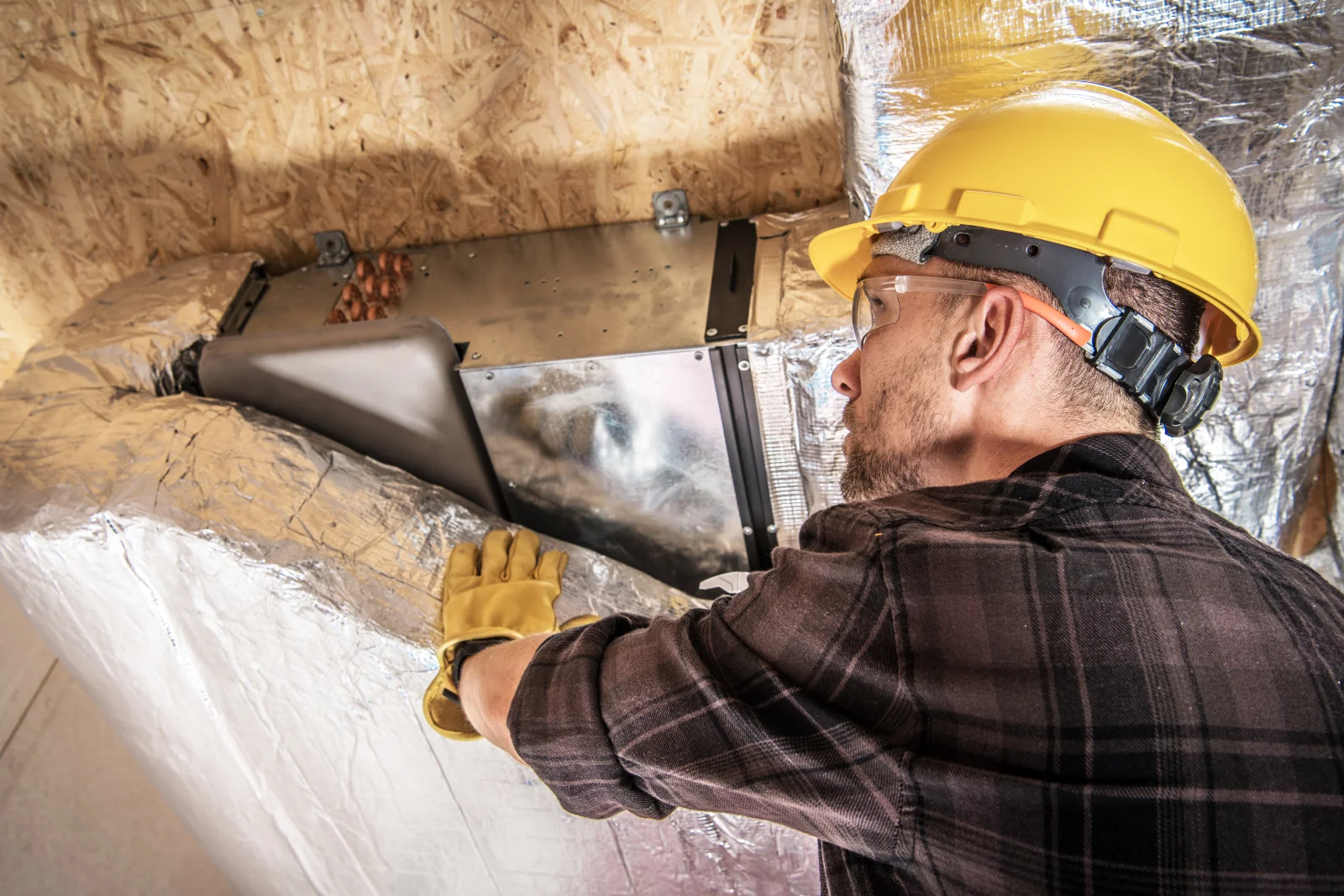 An HVAC technician inspecting damaged, insulated ductwork inside a Phoenix attic to find the source of lost airflow.