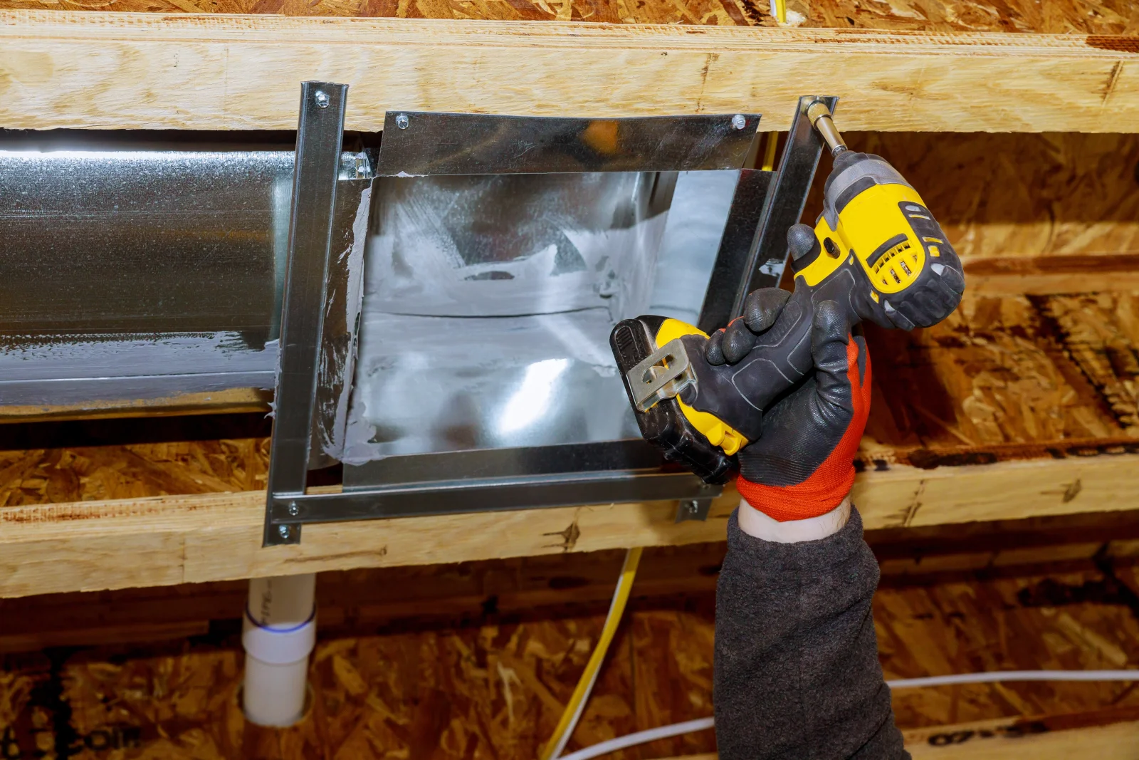 An HVAC technician reconnecting a disconnected duct boot to floor-joist framing during a Phoenix duct repair.