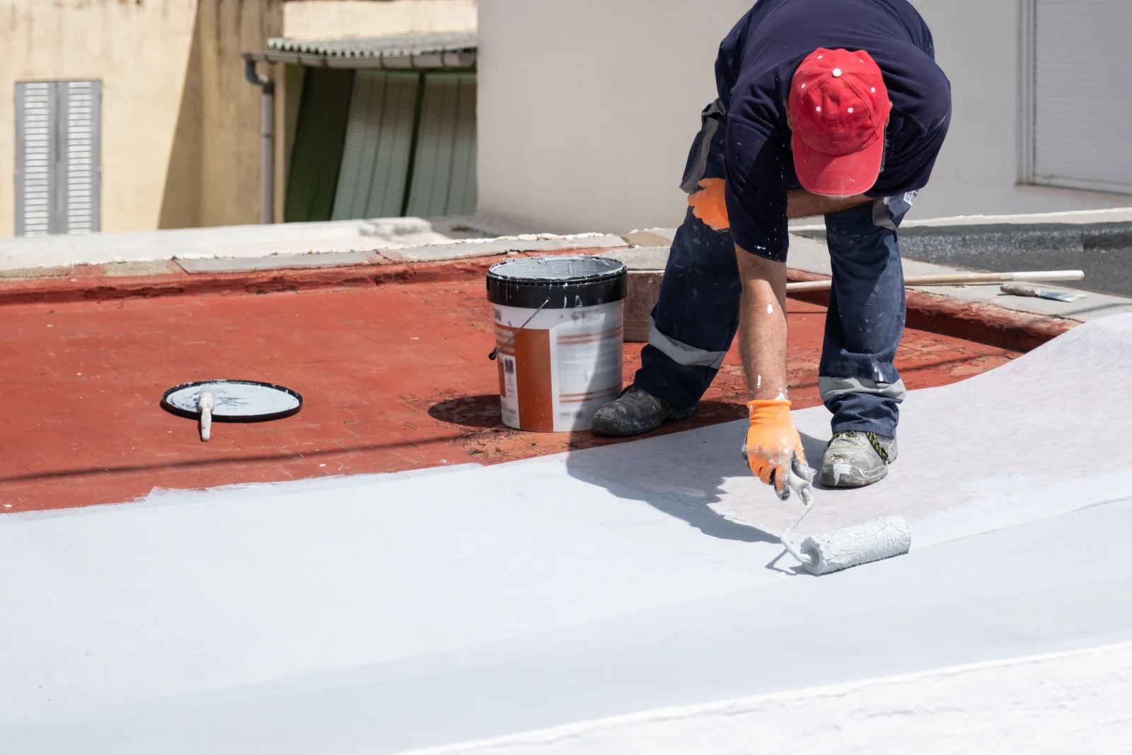 A roofing technician rolling reflective white elastomeric coating onto a flat residential roof in Phoenix, Arizona under full desert sun.