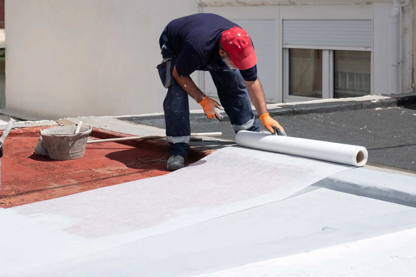 A roofing technician rolling out reinforcing base membrane on a Phoenix flat roof as part of prepping the surface before the reflective topcoat goes on.