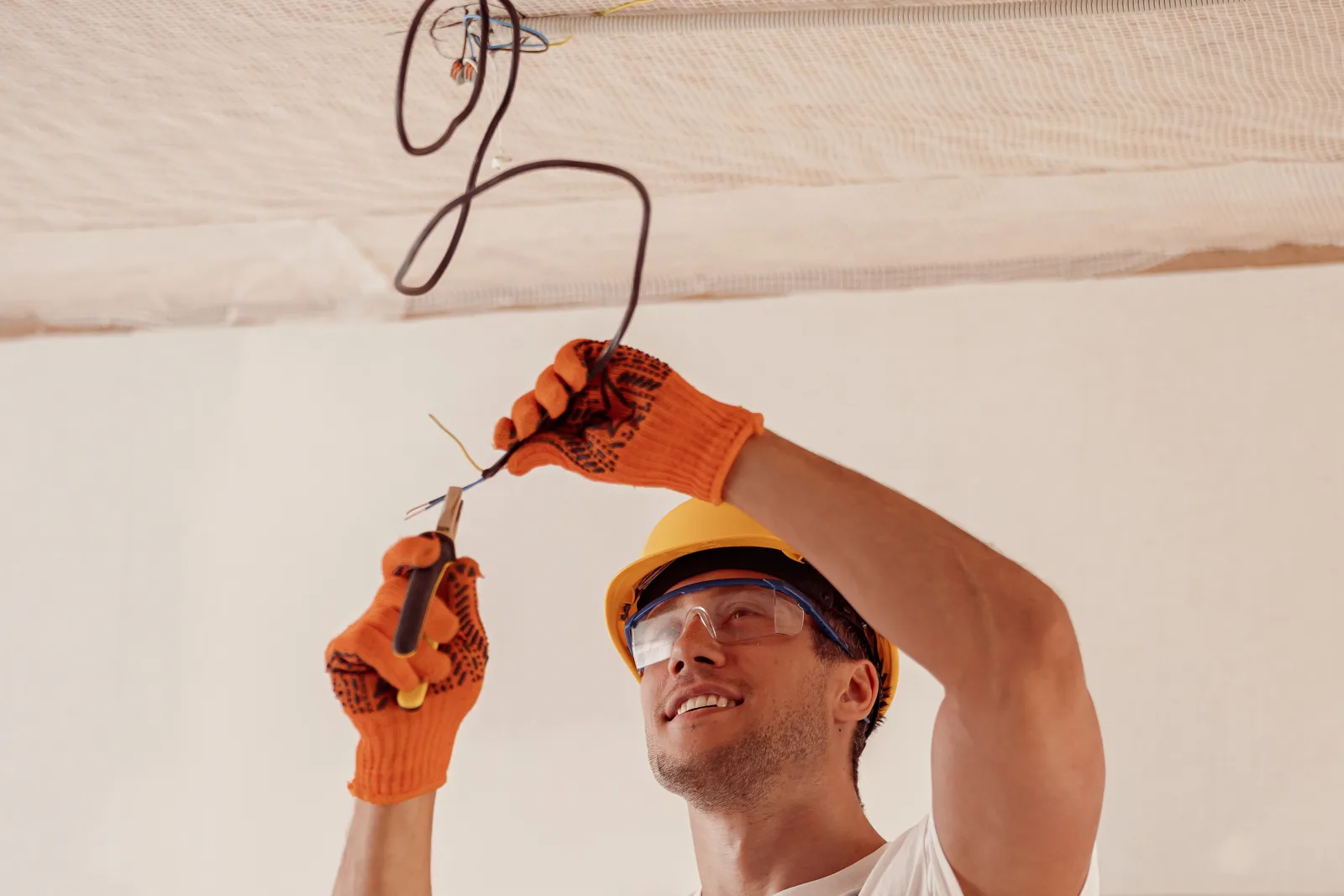 Electrical inspection in Phoenix, Arizona — an electrician in a hard hat and safety glasses checking wiring near the attic ceiling.