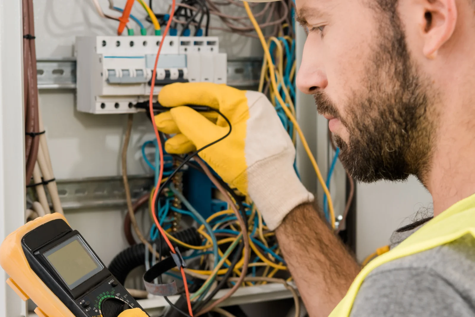 Electrical repair in Phoenix, Arizona — an electrician in a hard hat and gloves testing wiring in a breaker panel with a multimeter.
