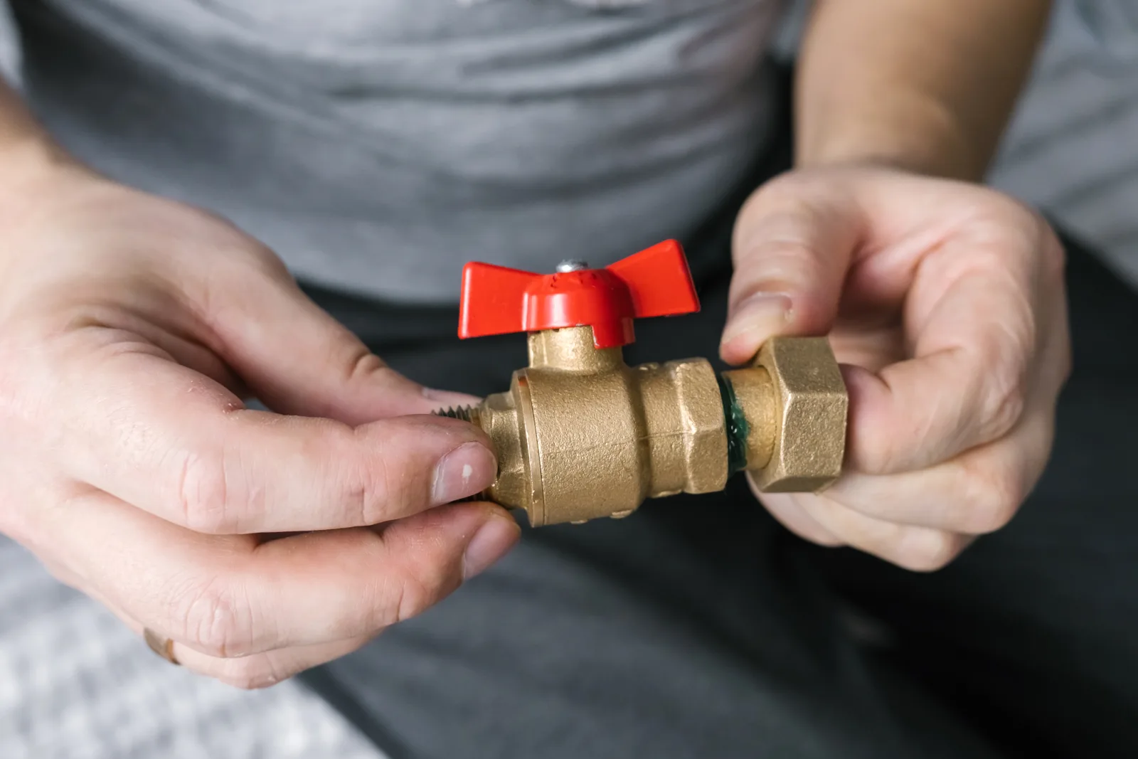 Hands turning off a brass water shutoff valve, the first step a Phoenix homeowner should take during a plumbing emergency.