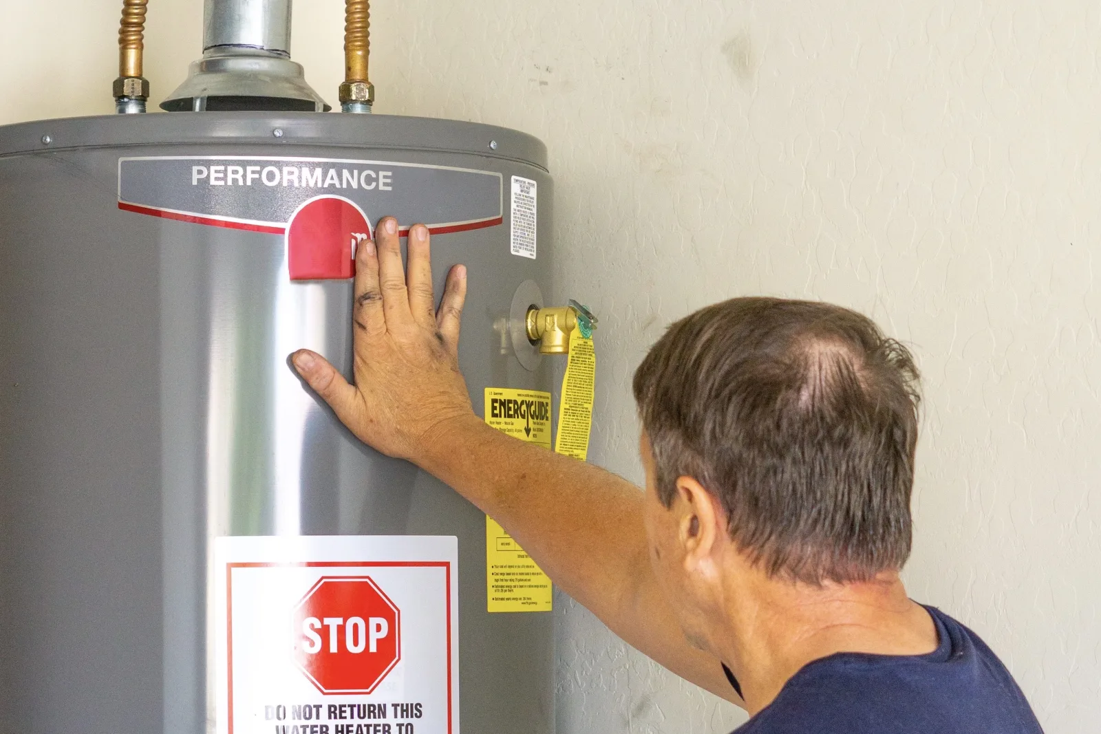 A technician inspecting a gas storage water heater in a Phoenix home garage, checking the control valve and connections for the corrosion and hard-water damage that cause plumbing emergencies.