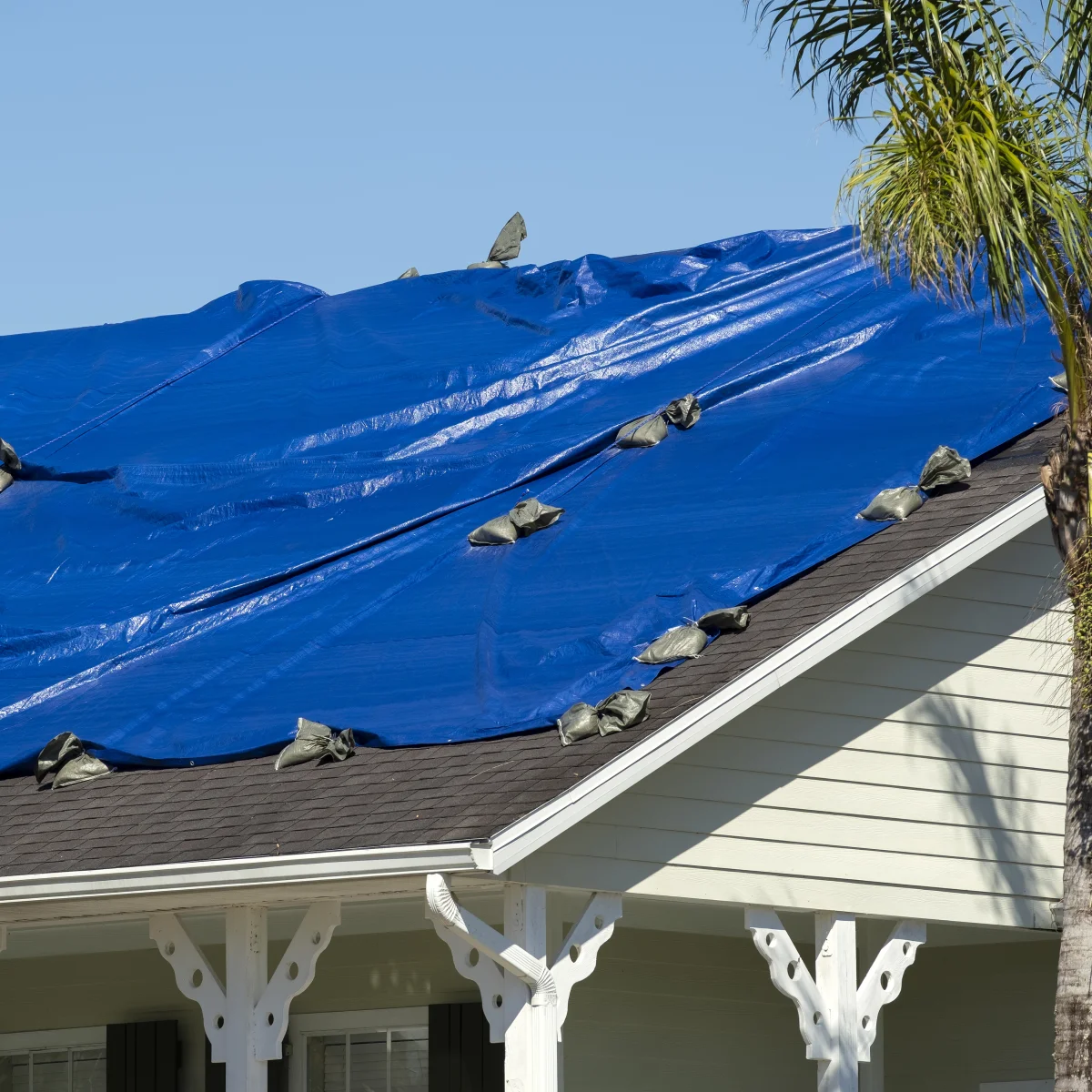 emergency-roof-repair-phoenix-storm-tarp Emergency roof repair in Phoenix, Arizona — a heavy-duty blue tarp sandbagged over a storm-damaged roof to stop an active leak.