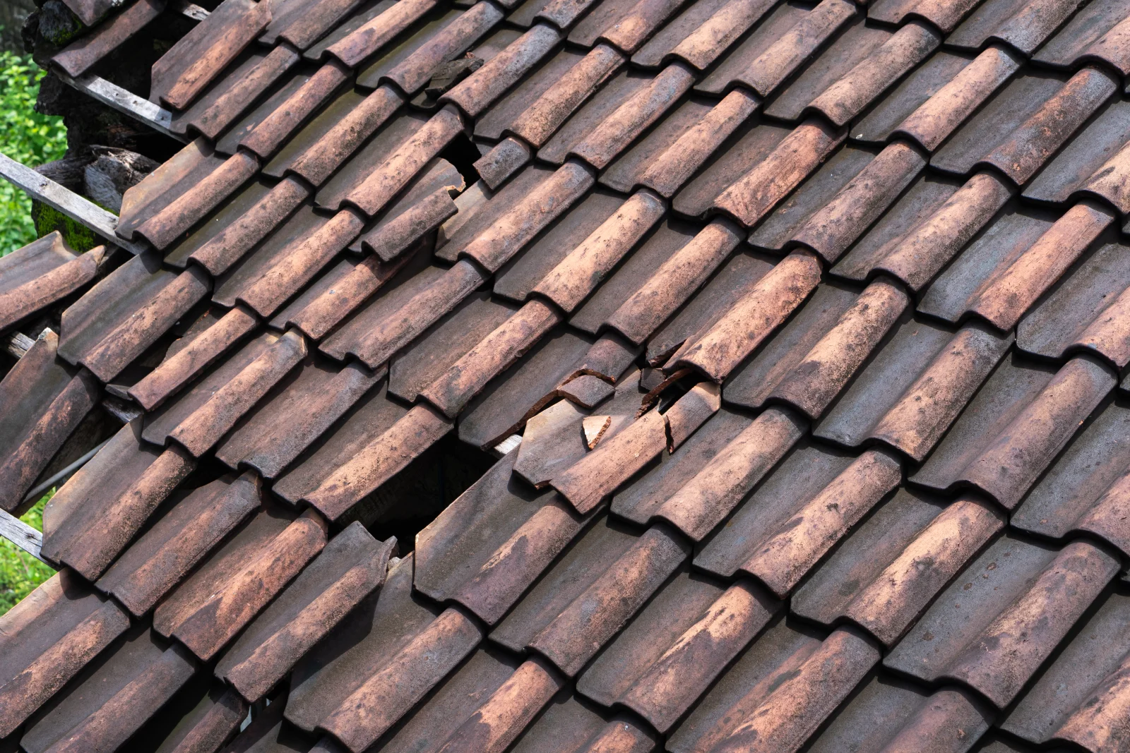 emergency-roof-repair-phoenix-monsoon-damage A close-up of cracked and broken clay roof tiles after a monsoon storm, the kind of wind and water damage an emergency roof repair pro tarps and repairs before the next rain.