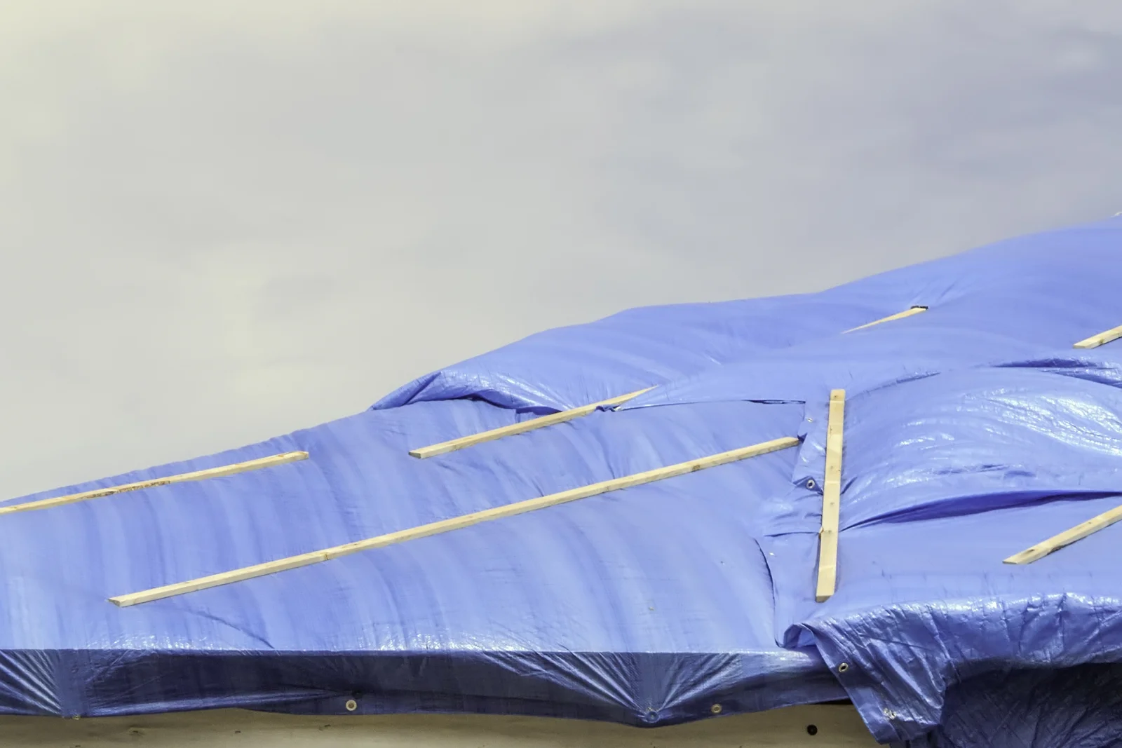emergency-roof-repair-phoenix-tarp-dry-in A heavy-duty blue tarp secured with wooden strips and sandbags over a storm-damaged section of roof to stop an active leak, the temporary dry-in step an emergency crew does before a permanent repair once the roof is dry.