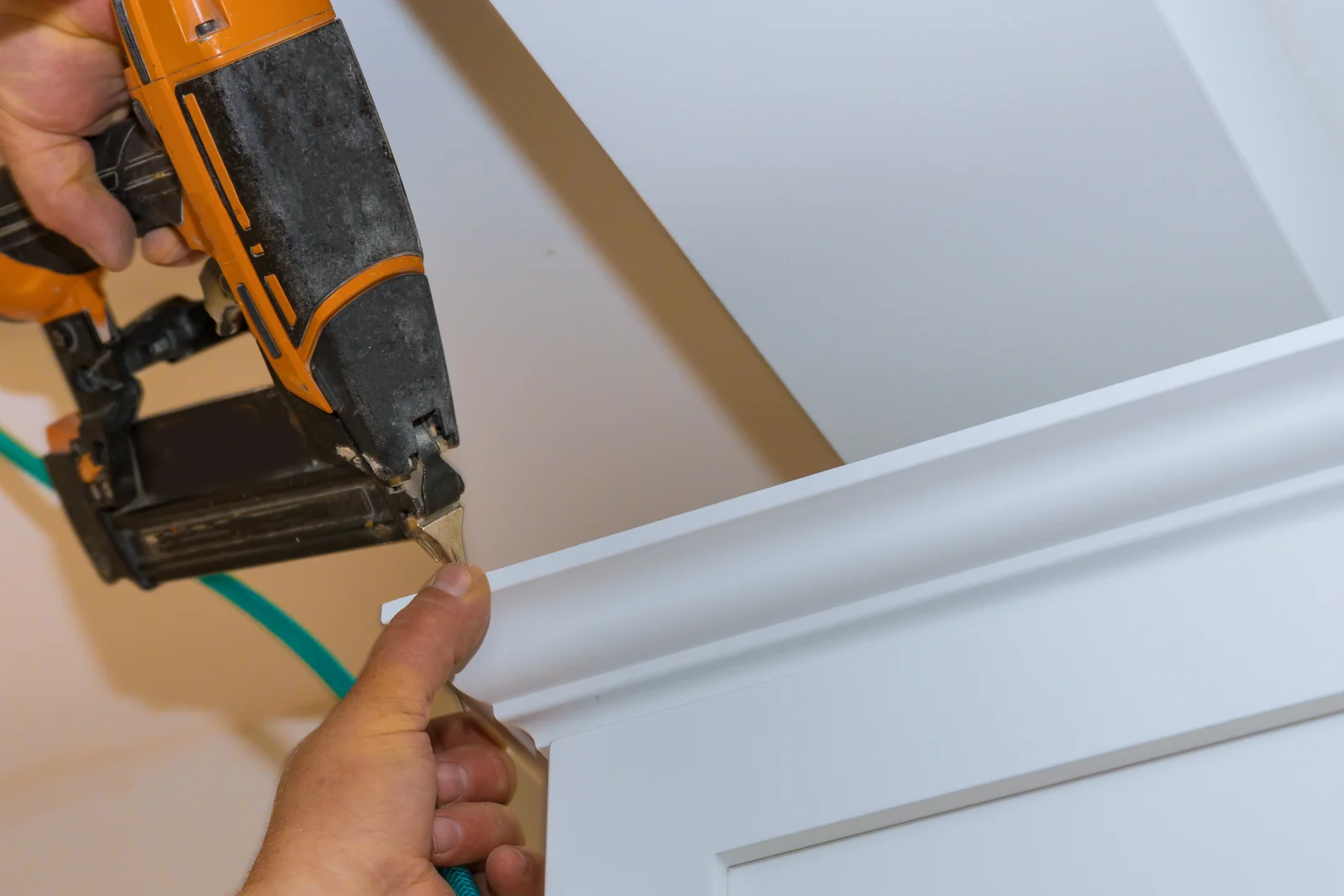 finish-carpentry-phoenix-crown-molding A finish carpenter using a nail gun to install crown molding with a clean mitered corner in a Phoenix home.