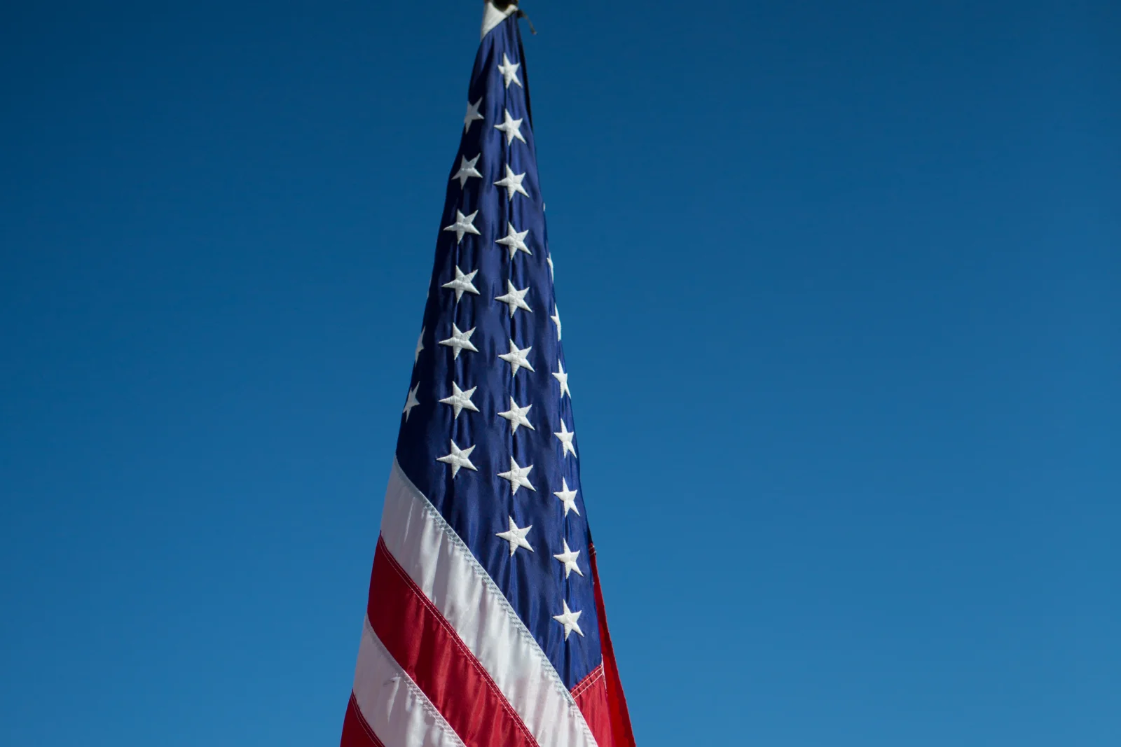 Close-up of an American flag on a flagpole against a clear blue Phoenix, Arizona sky, showing the fabric and stitching built to hold up in intense desert sun.
