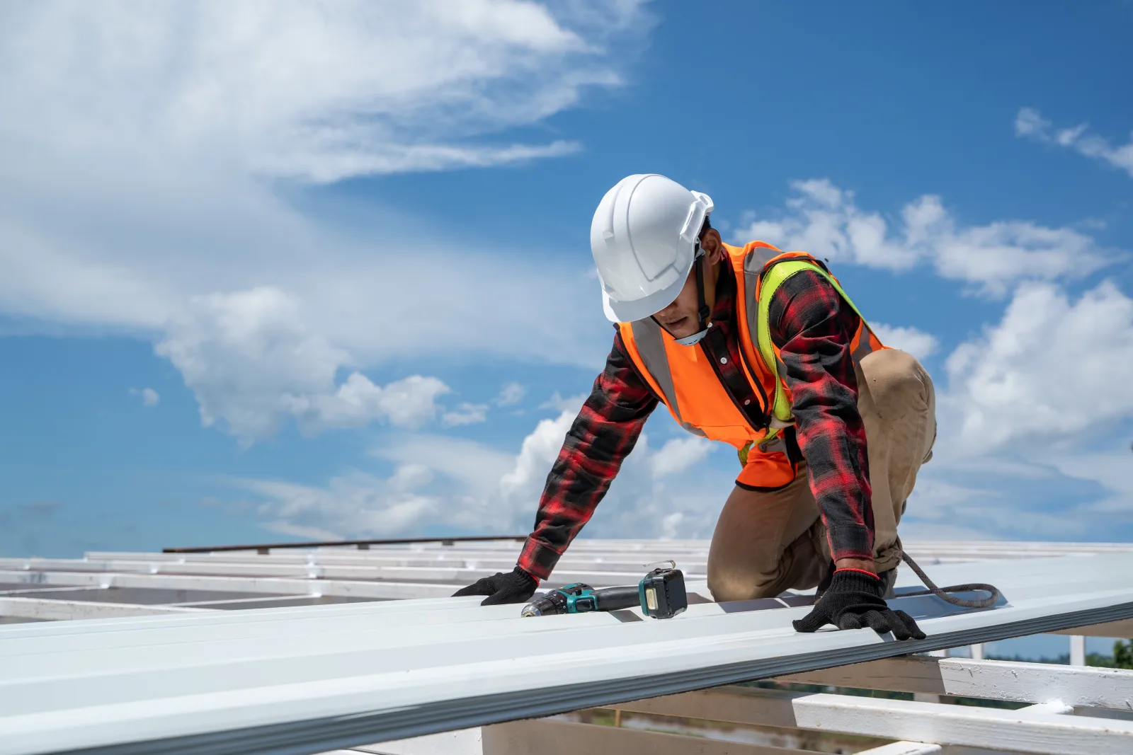 Flat roof installation in Phoenix, Arizona — a roofer in a hard hat and safety vest installing a white reflective membrane roof under a sunny sky.