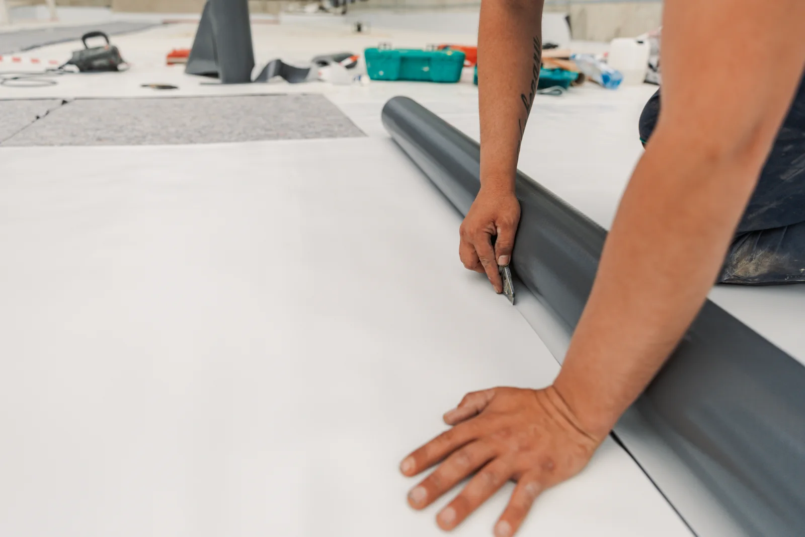 flat-roof-replacement-phoenix-new-tpo-membrane A roofer's hands cutting and fitting a new white TPO membrane roll into place, the seam-and-cut work of installing a new flat roof system during a Phoenix replacement.